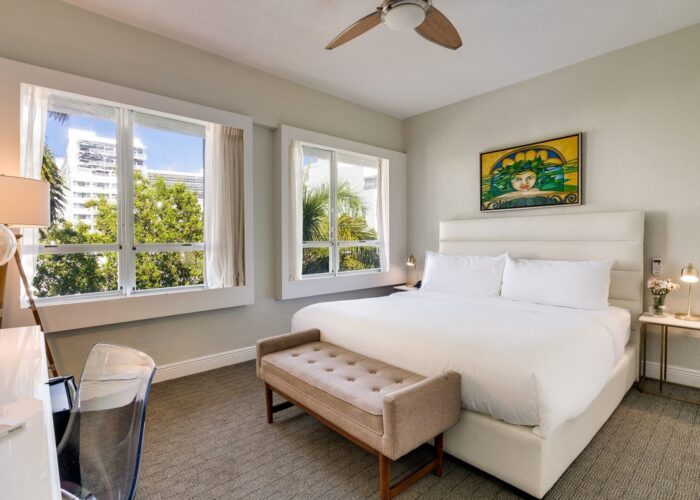 Bed with a tan bench under a ceiling fan by bright windows in Accessible Standard King Bedroom at Crest Hotel & Suites