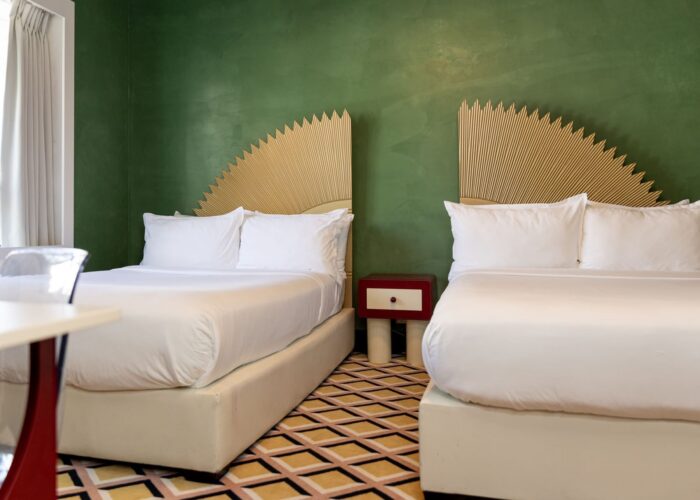 Two queen beds with sunburst headboards and a small side table in the Eclectic Double Room at Crest Hotel & Suites
