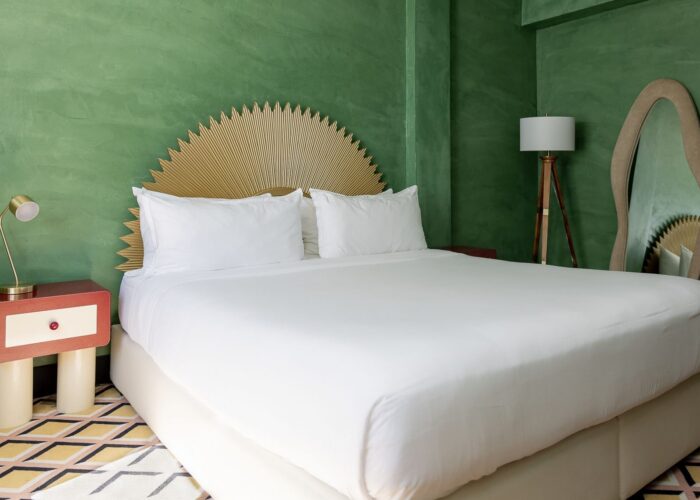 Bed with a fan-shaped headboard by a red and white nightstand in Eclectic King at Crest Hotel & Suites