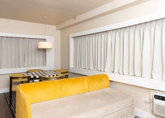 Yellow sofa by a striped dining table near a window in One Bedroom Suite at Crest Hotel & Suites