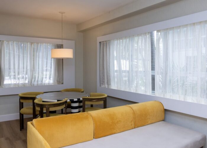 Velvet yellow sofa and round striped table by the large draped windows in One Bedroom Suite at Crest Hotel & Suites