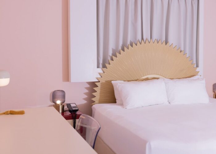 Bed with a sunburst headboard by a lamp and phone on a red nightstand in Standard King at Crest Hotel & Suites