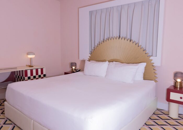 Bed under a gold sunburst headboard surrounded by nightstands on a geometric rug in Standard King at Crest Hotel & Suite