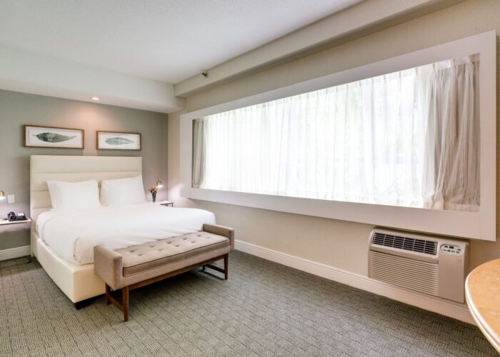 Bed with a tufted bench beside the large curtained window in the Standard Queen Room at Crest Hotel & Suites