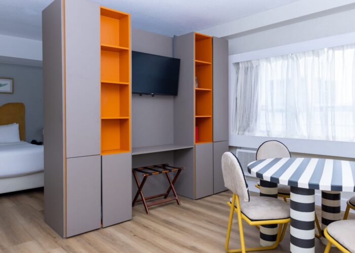 Round striped dining table with matching chairs next to a grey shelving unit in Studio Double at Crest Hotel & Suites