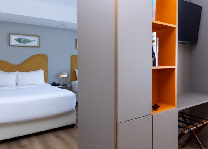 Grey and orange storage divider unit near a plush guest bed in the Studio Double Room at Crest Hotel & Suites