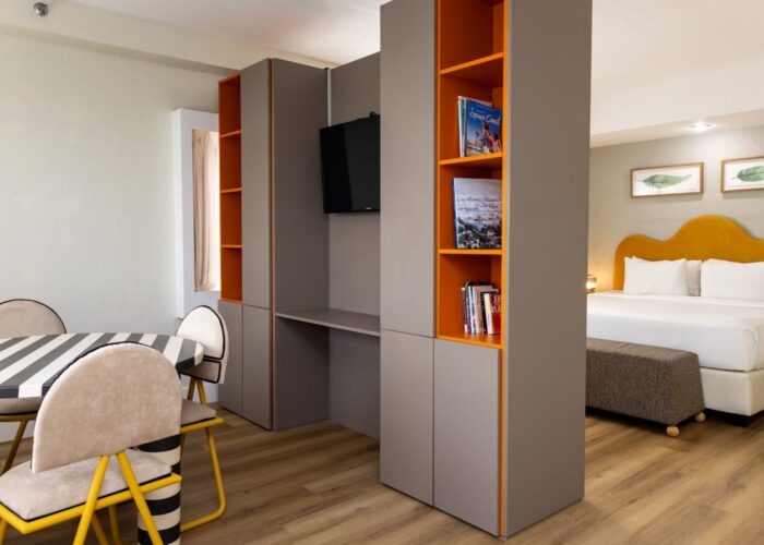 Grey and orange storage divider unit separating a striped dining table in Studio King at Crest Hotel & Suites