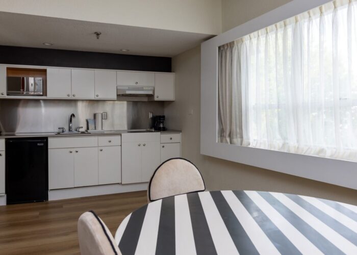 Modern kitchen space with a mini fridge near a striped breakfast table inside the Studio King Room at Crest Hotel & Suit